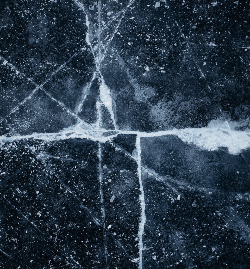 Dark lake ice crossed by white cracks